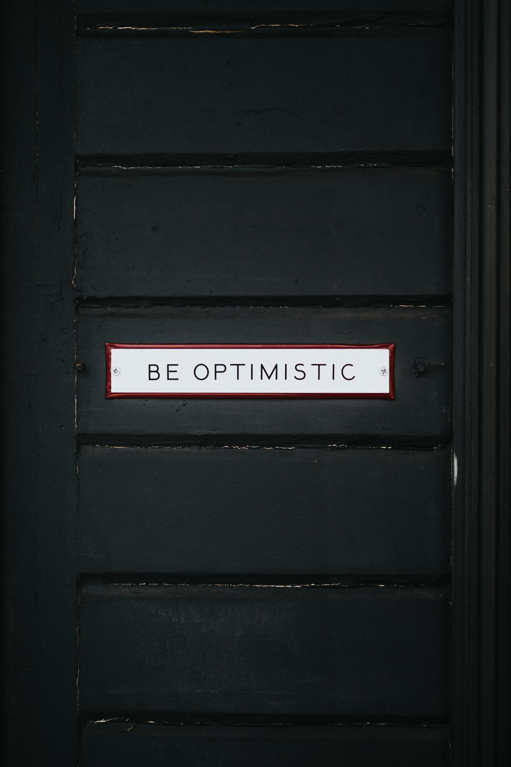 Black door with sign "Be Optimistic"